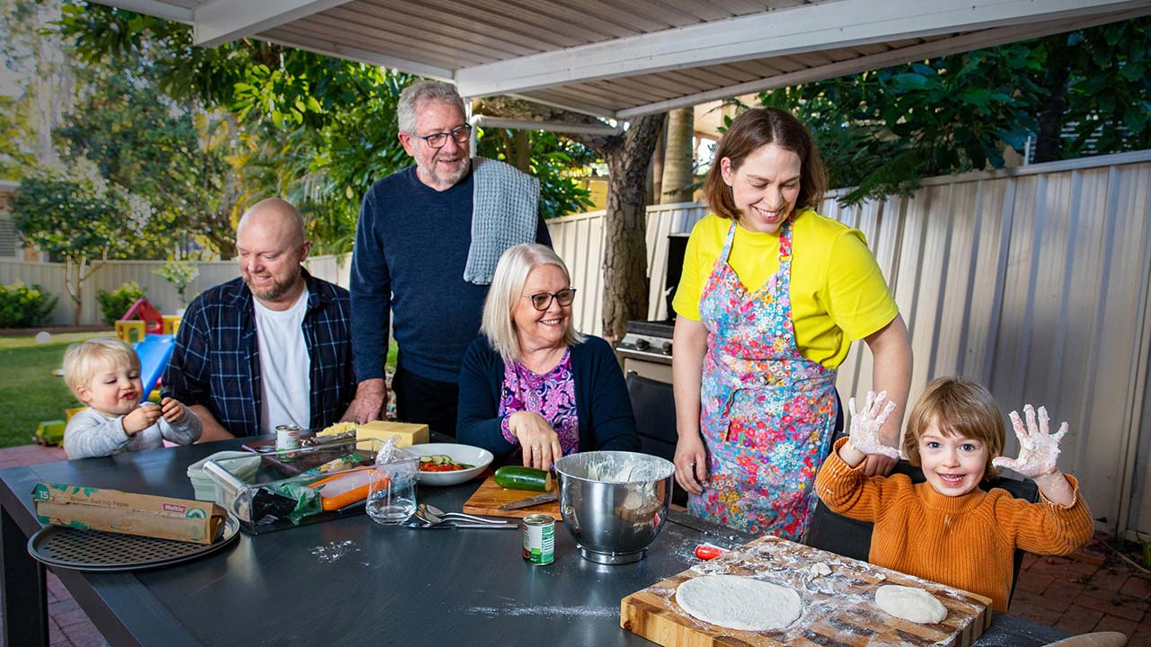 A family is gathered around a table outside. They are preparing lunch. 