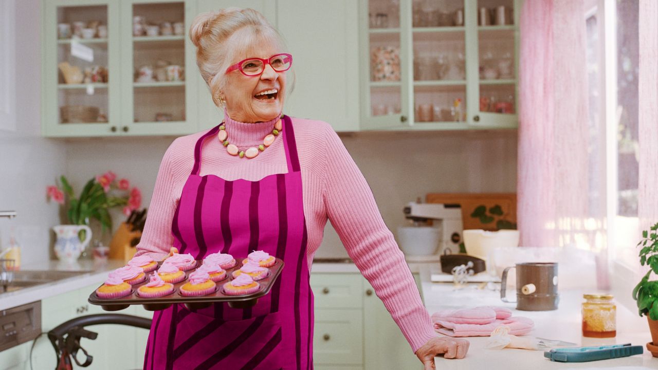 Senior woman in a kitchen holding a tray of cupcakes and enjoying her baking time Senior woman in a kitchen holding a tray of cupcakes and enjoying her baking time