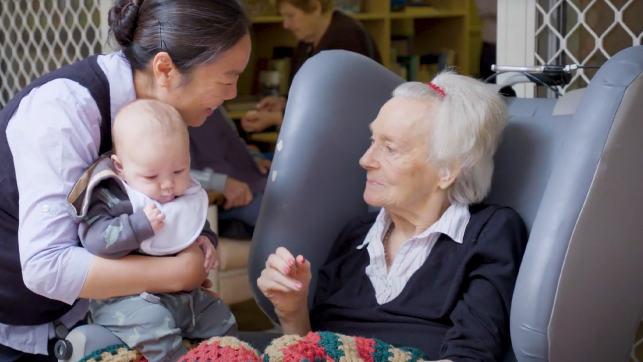 An older woman holding a small baby, both are smiling and happy.