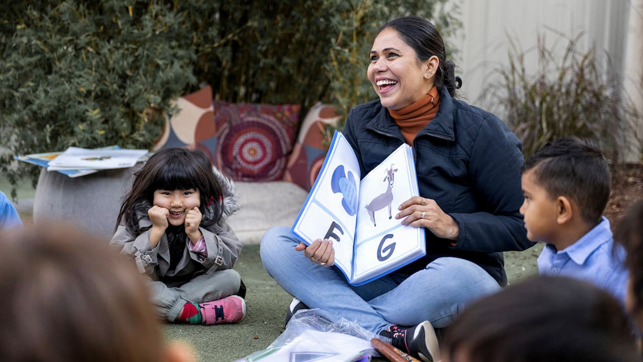 Educator showing children alphabet book outside.