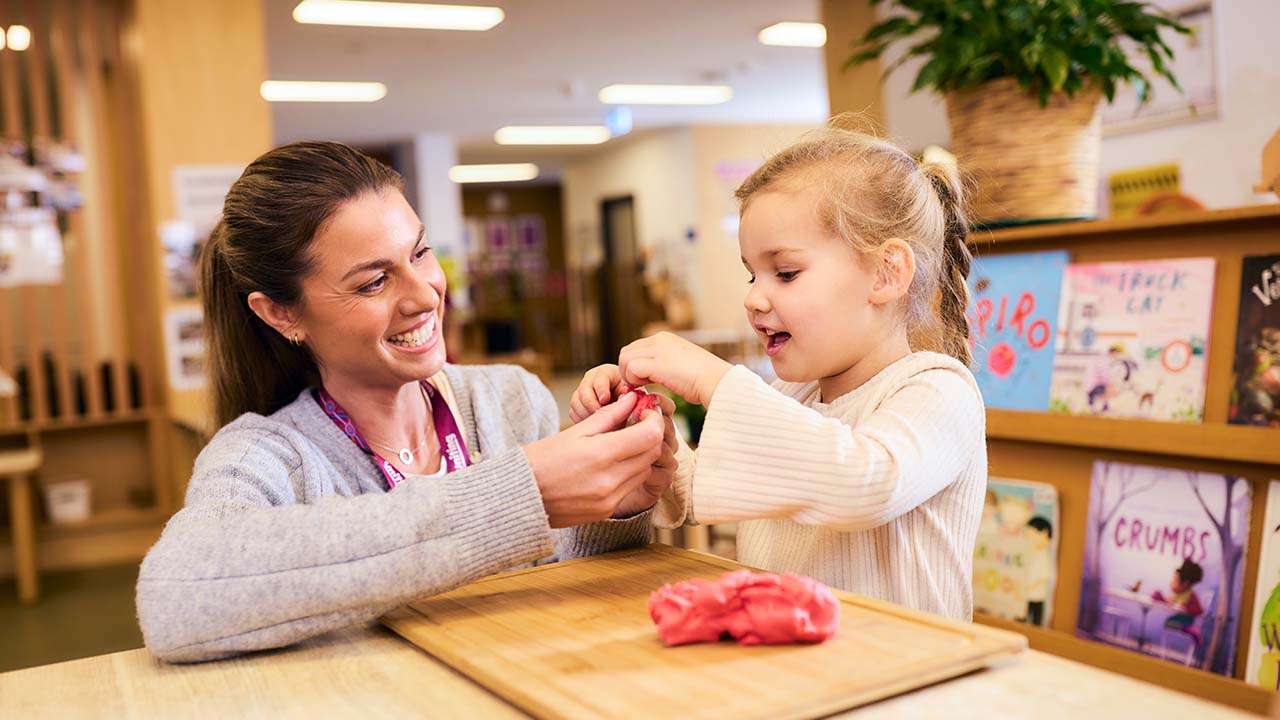 Educator sitting with child who is playing with playdough.