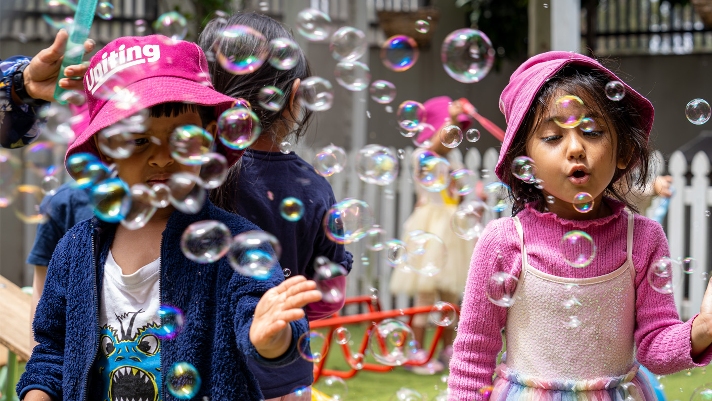 Two children blowing and popping bubbles outside.