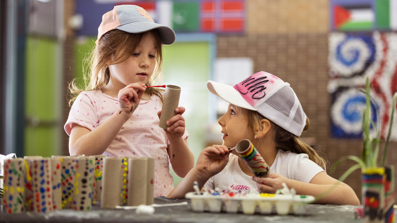 Two children painting on cardboard rolls.