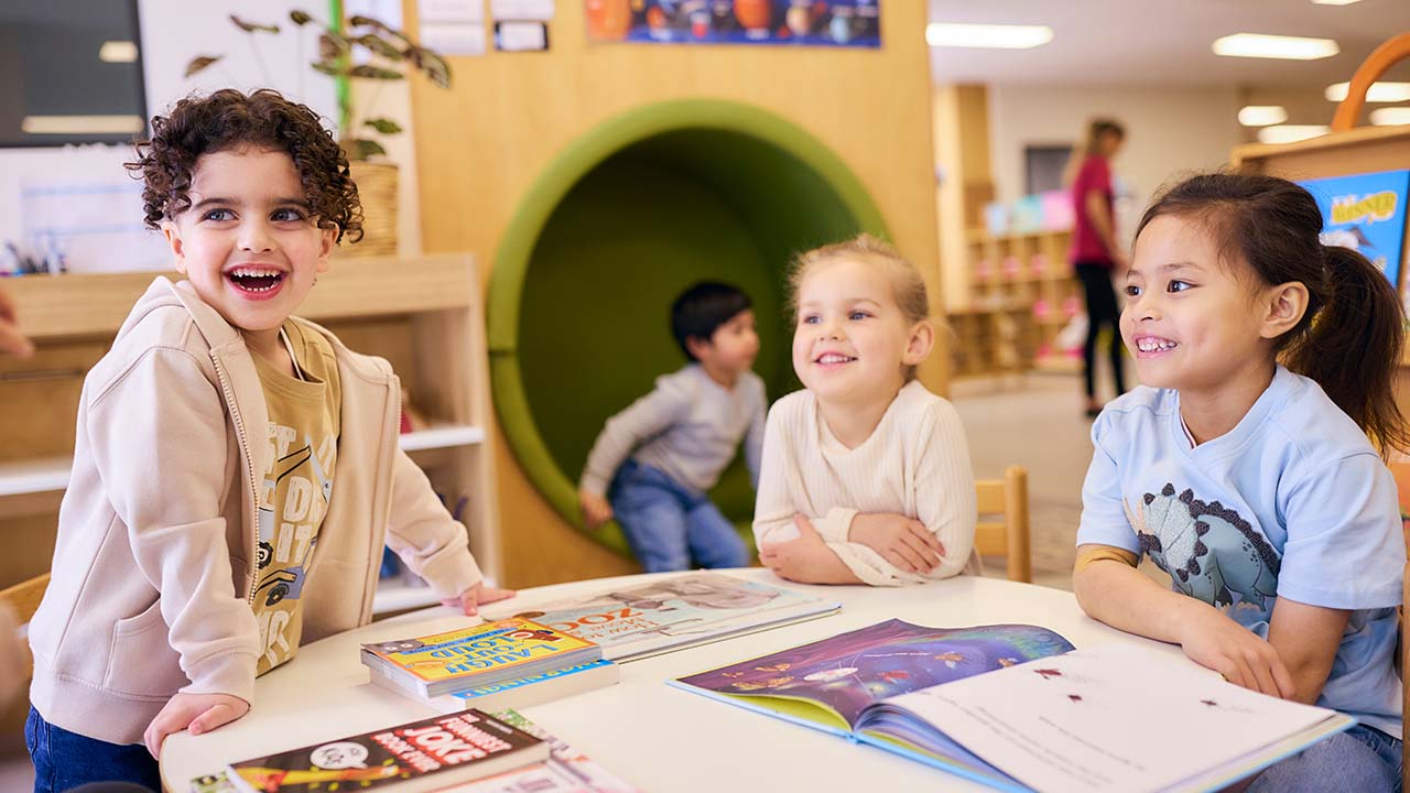Children looking at books in classroom and smiling.