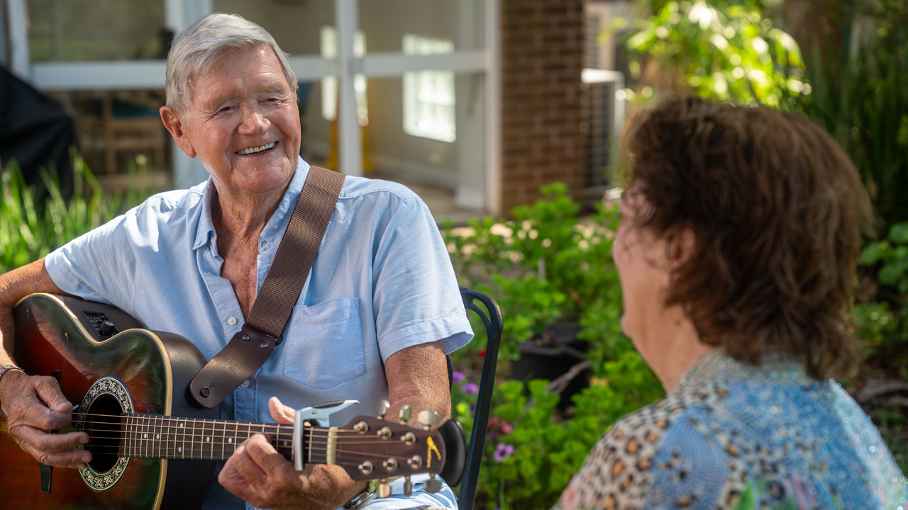 Senior man playing a guitar for a woman outside Senior man playing a guitar for a woman outside