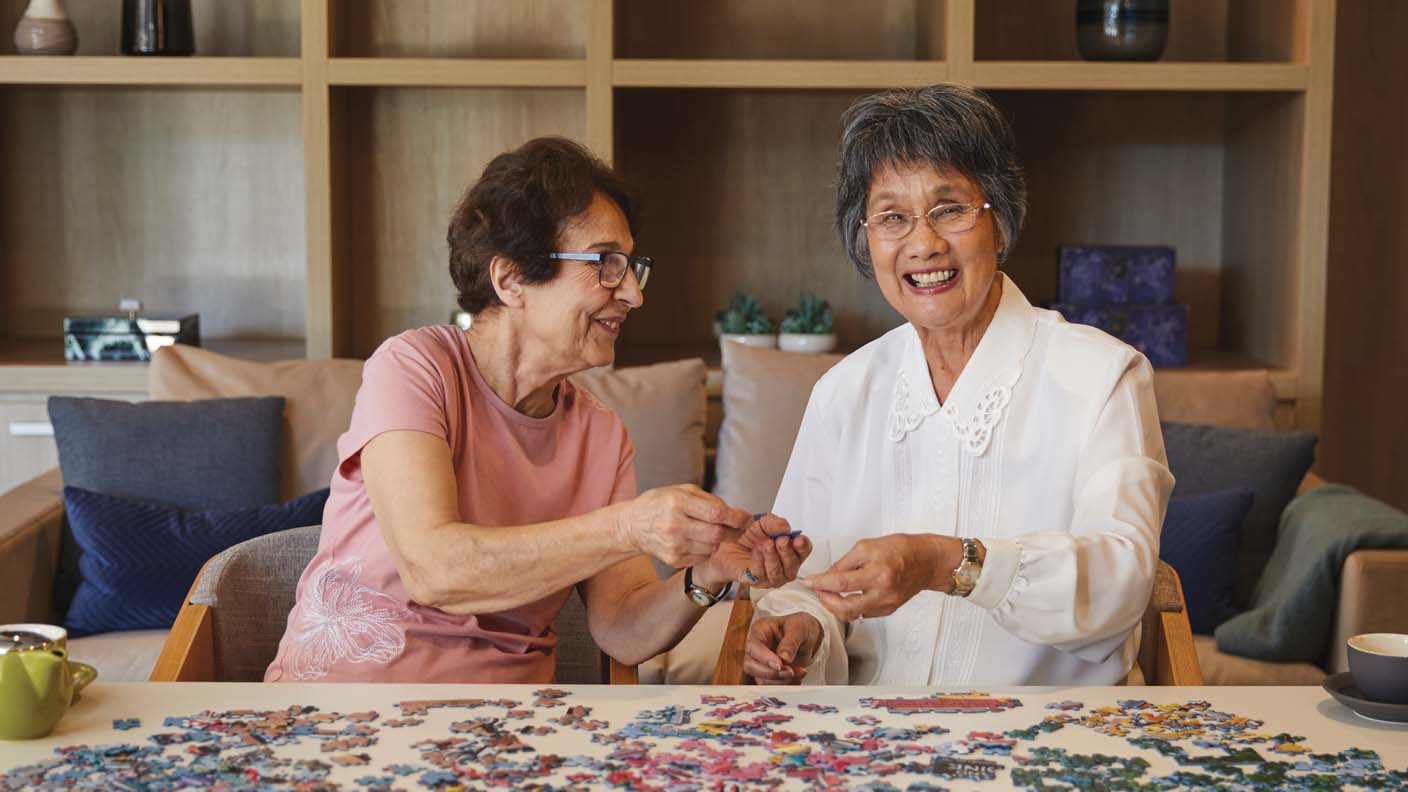 Two seniors are completing a puzzle together.