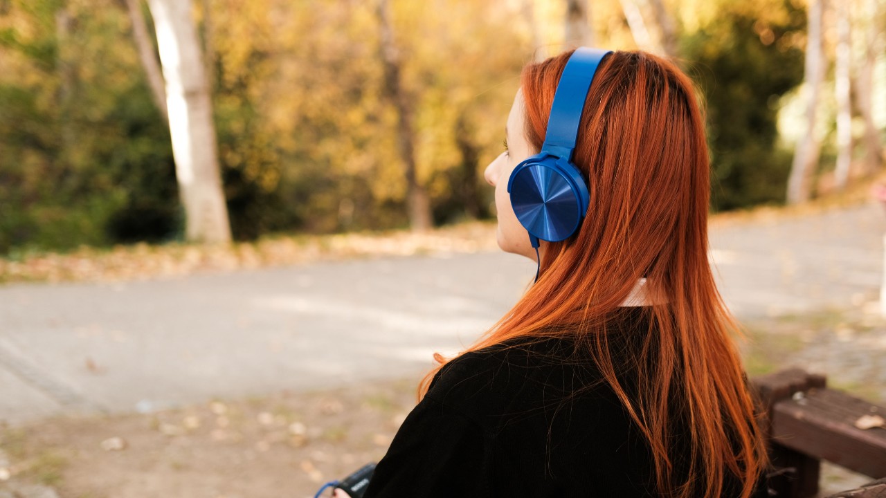 A young person is sitting on a park bench, wearing headphones.